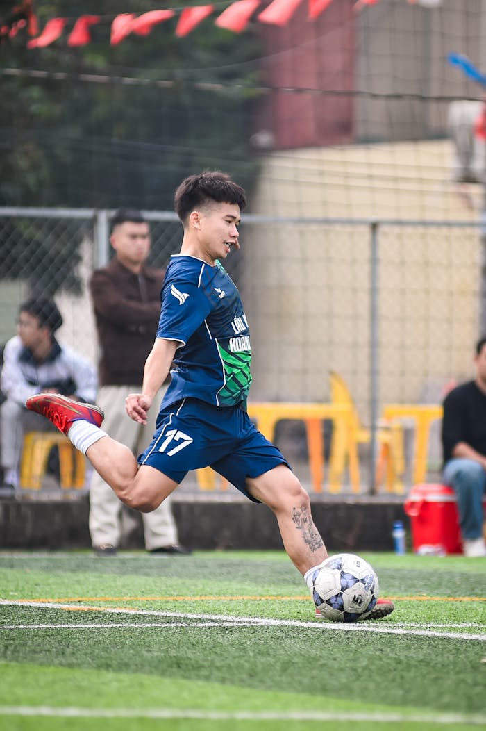 Dynamic portrait of a football player kicking a ball on a grassy field.